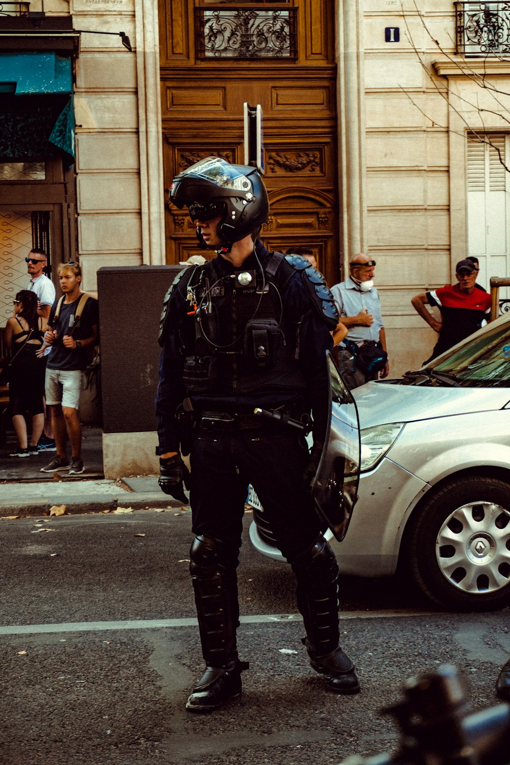 昼間、白い車の横に立つ黒い警官の制服を着た男
