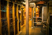 A dimly lit server room with multiple racks of computer servers surrounded by cables and various technical equipment. The space has an industrial feel with visible pipes and ductwork, and a sign on one rack stating 'Do not use'.