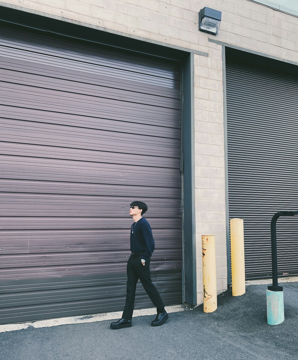 man in black jacket and black pants standing near roll up door