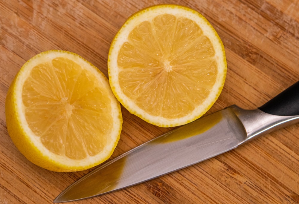 in Scheiben geschnittene Zitrone neben silbernem Messer auf braunem Holztisch