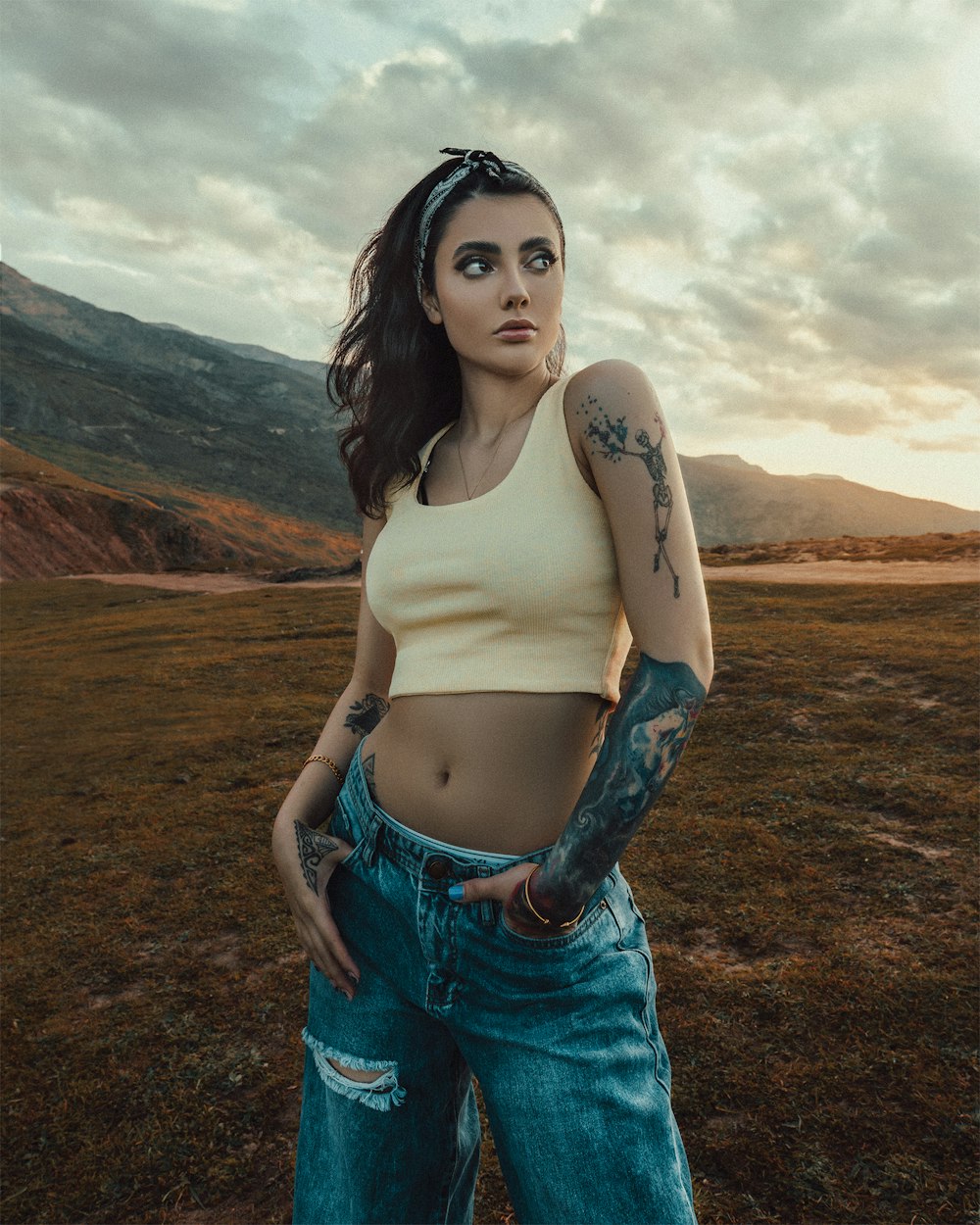 woman in white tank top and blue denim shorts standing on brown field during daytime