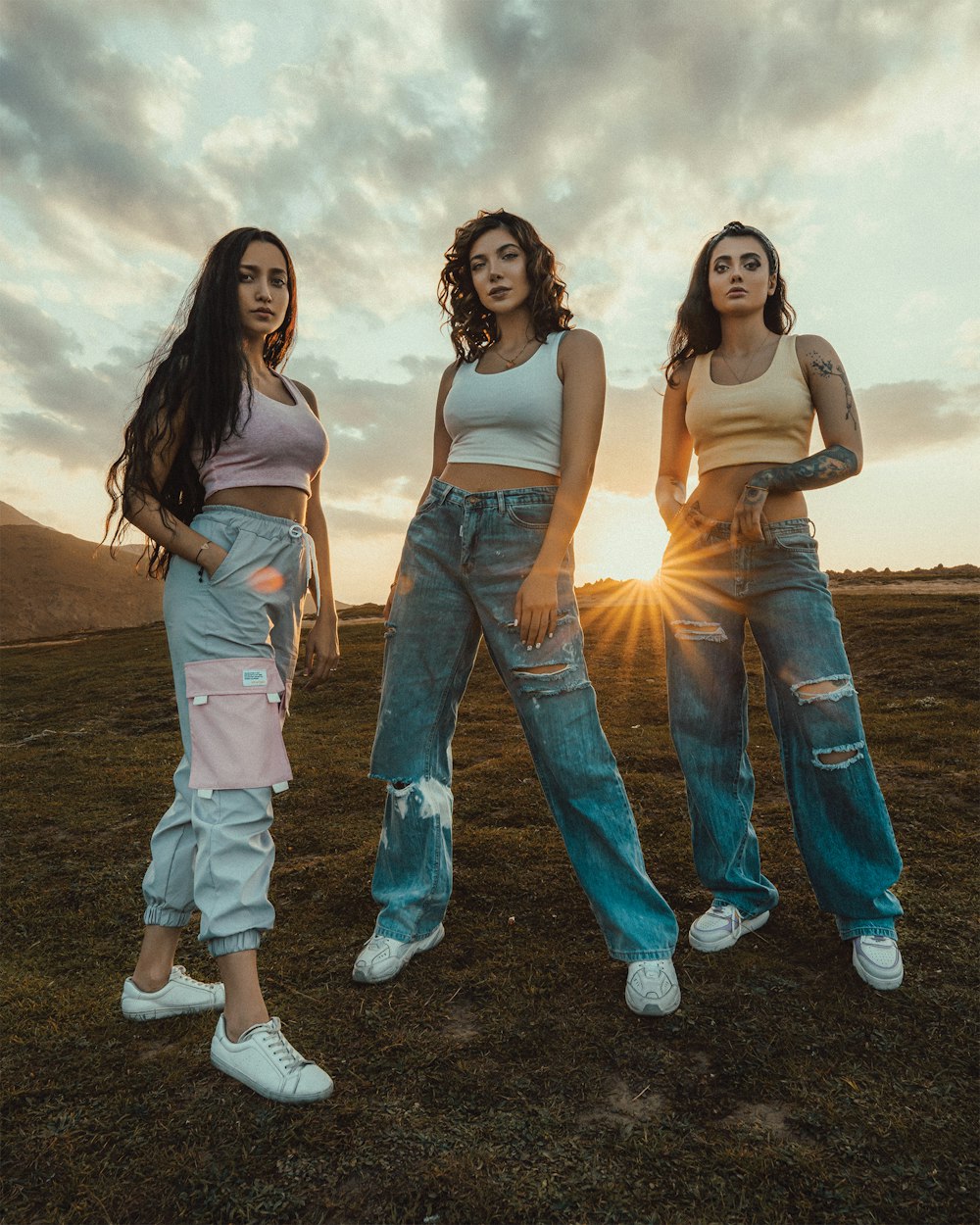 2 women in white tank top and blue denim jeans standing on brown field during daytime