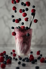 A vibrant glass of mixed berry smoothie surrounded by fresh strawberries and blueberries.