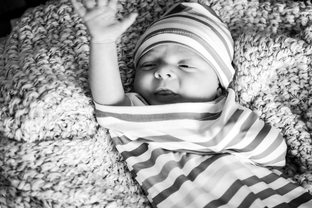 Foto en escala de grises de un bebé con camisa a rayas tirado en el suelo