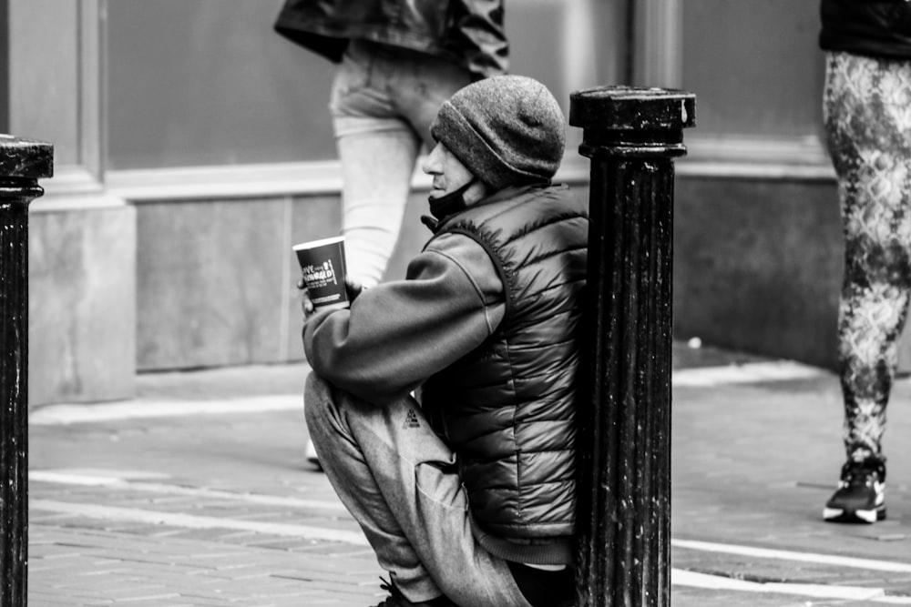 man in jacket and pants sitting on wooden post