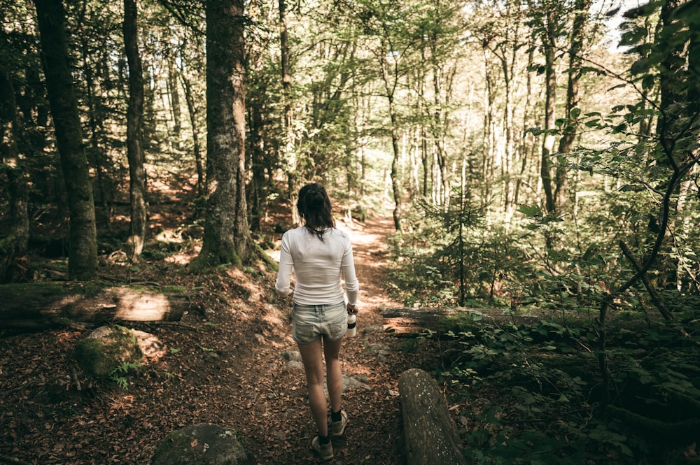 femme en t-shirt blanc et short blanc debout au milieu de la forêt pendant la journée