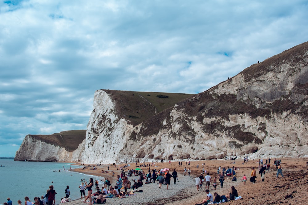 people on beach near brown mountain under blue sky during daytime