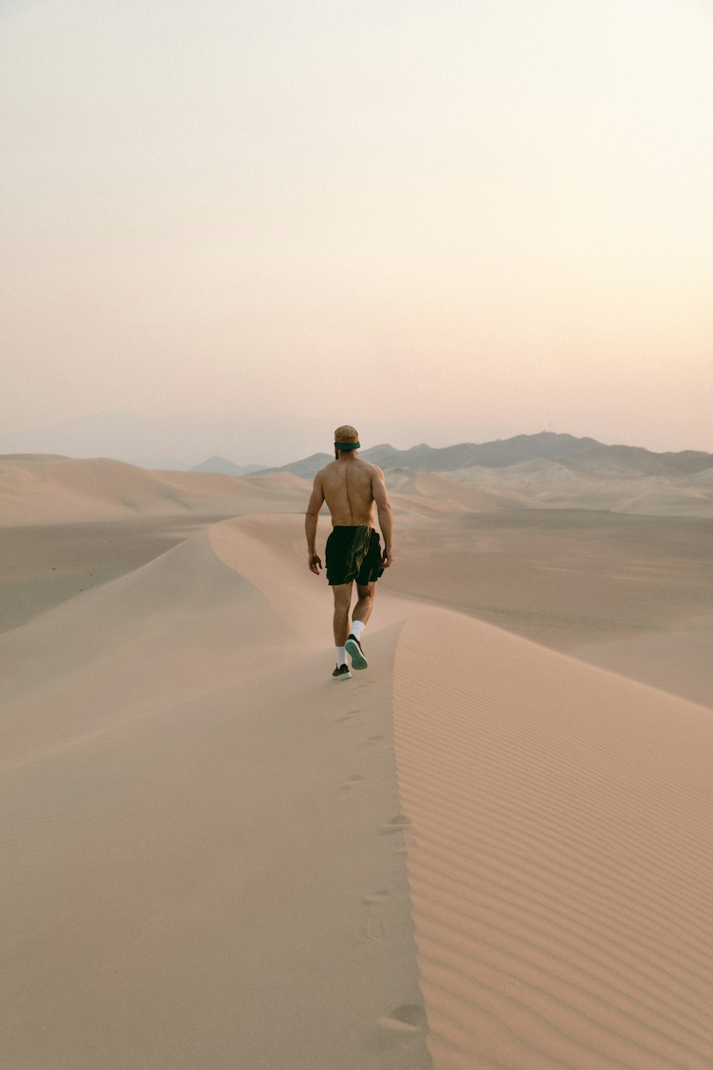 uomo in pantaloncini neri che cammina sul deserto durante il giorno
