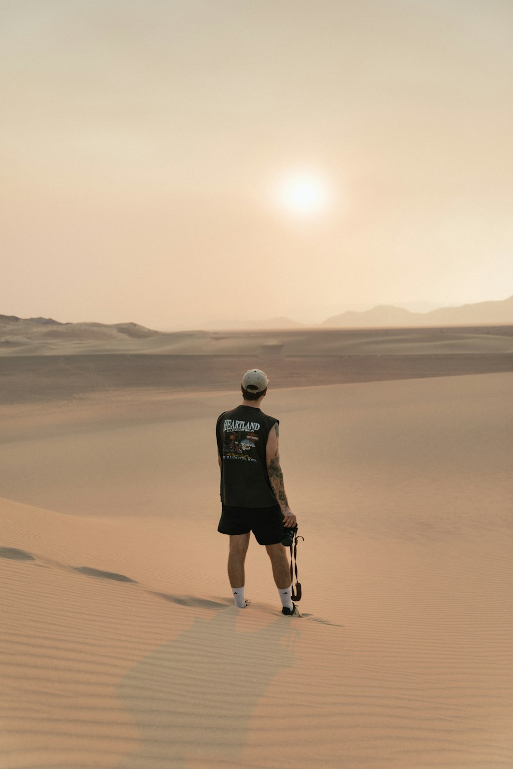 Mann in schwarzem T-Shirt und schwarzen Shorts geht tagsüber durch die Wüste