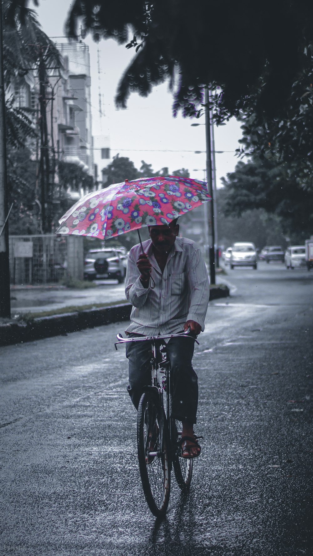 homem na jaqueta cinza que monta a bicicleta com guarda-chuva na estrada durante o dia