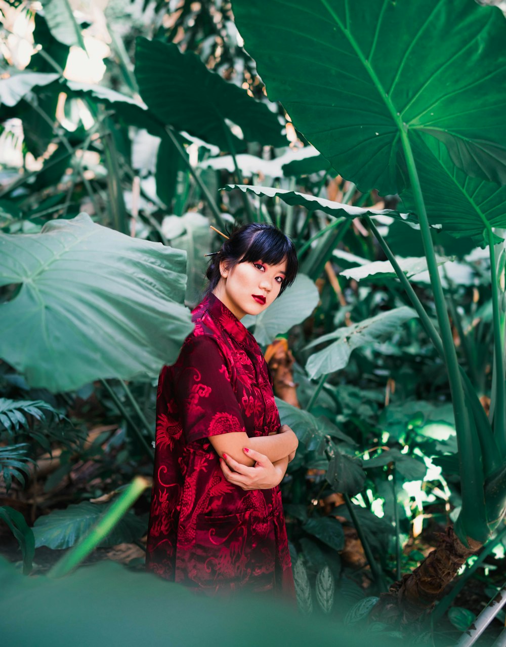 woman in red and white floral dress standing under green leaves during daytime