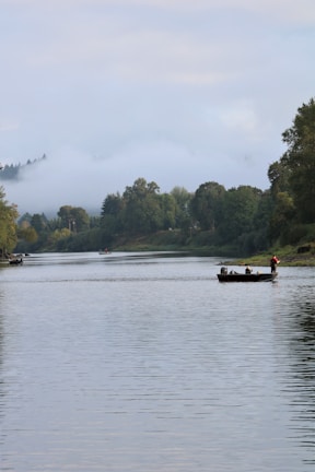 A fishing boat gently floating on the serene river at dawn, surrounded by lush greenery.