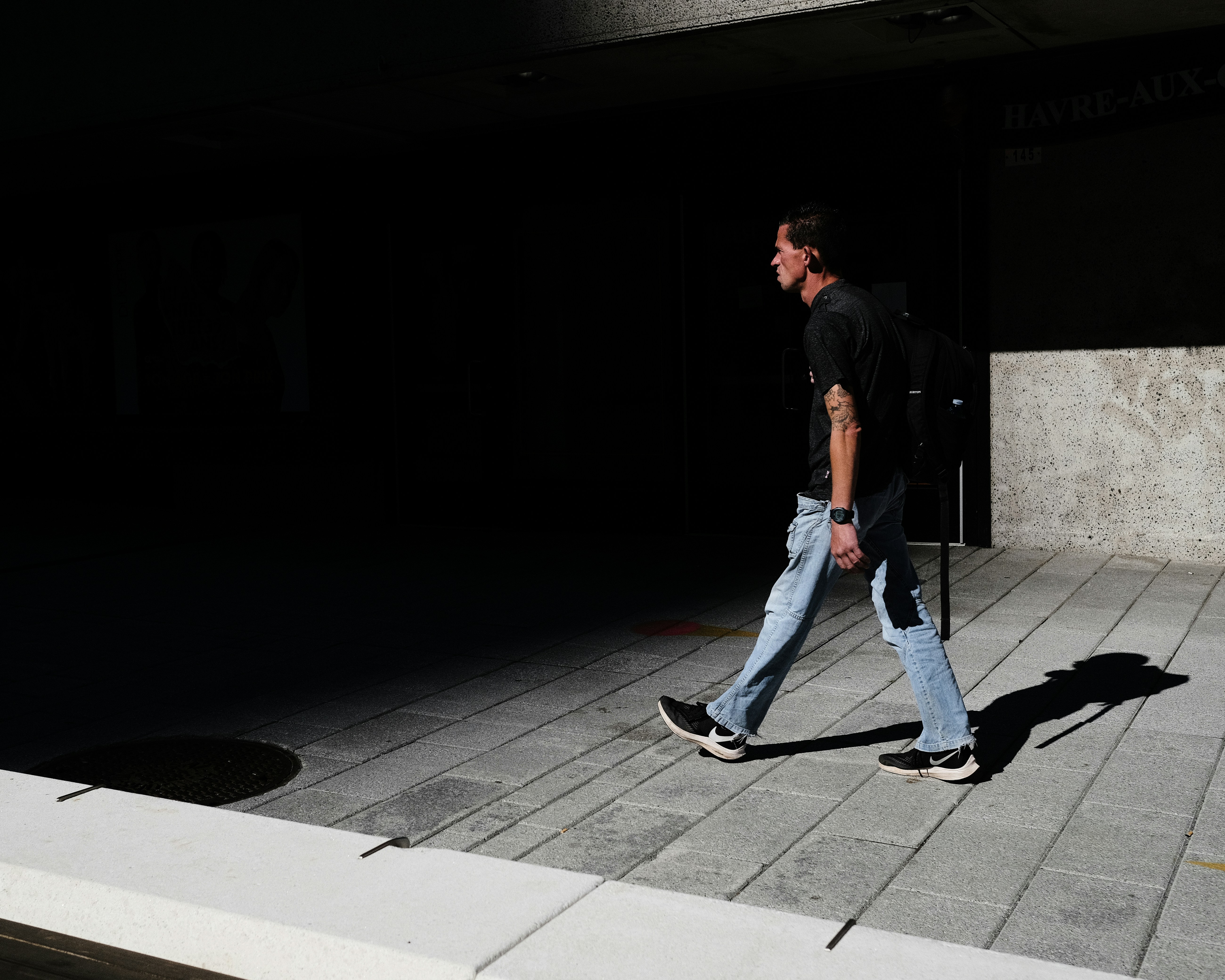 man in black t-shirt and blue denim jeans walking on sidewalk during daytime