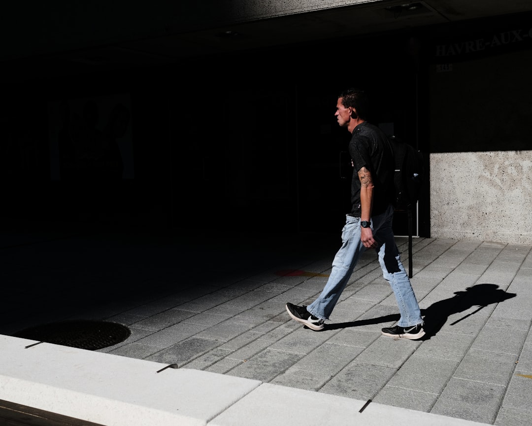 man in black t-shirt and blue denim jeans walking on sidewalk during daytime