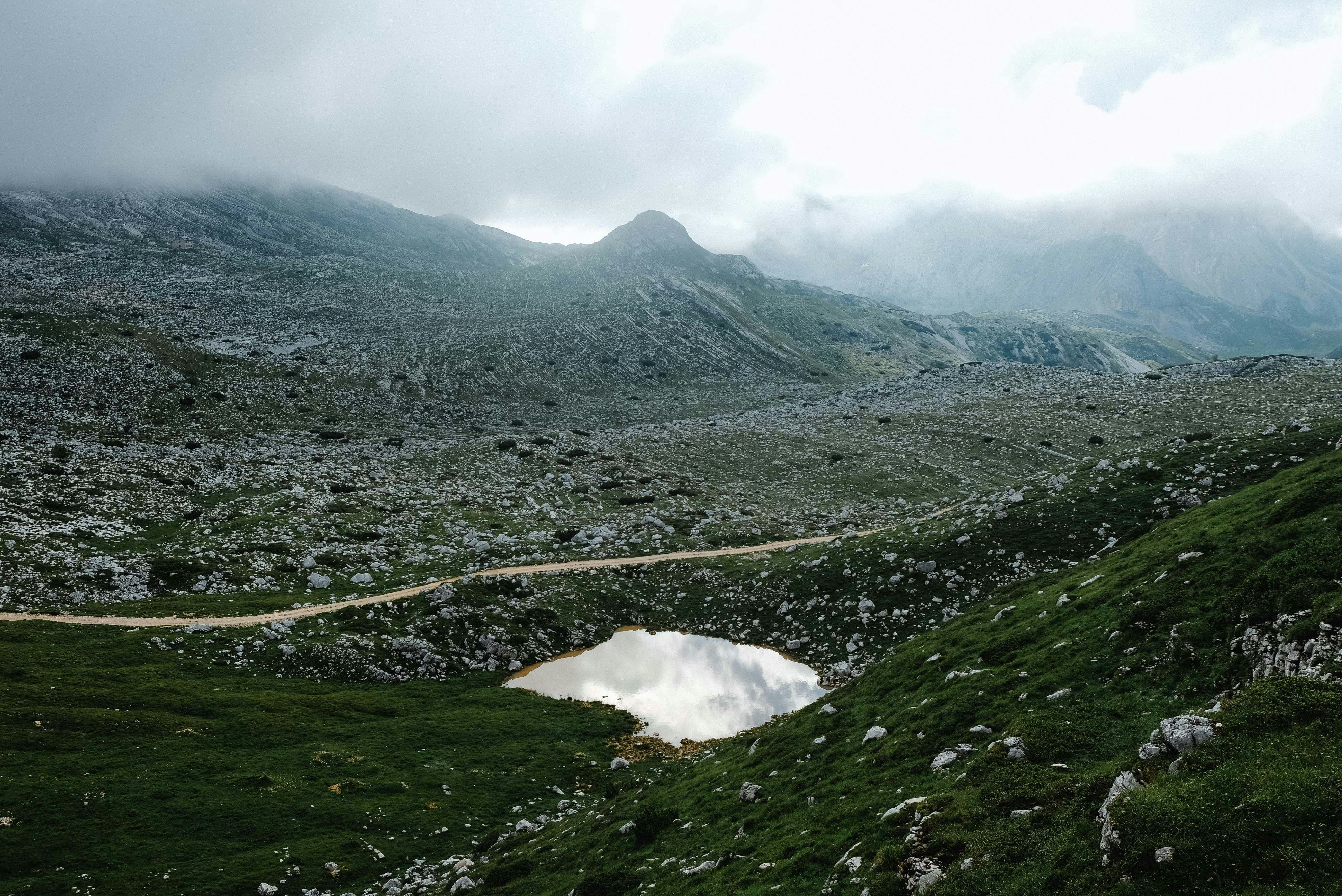 campo di erba verde e montagna sotto nuvole bianche durante il giorno