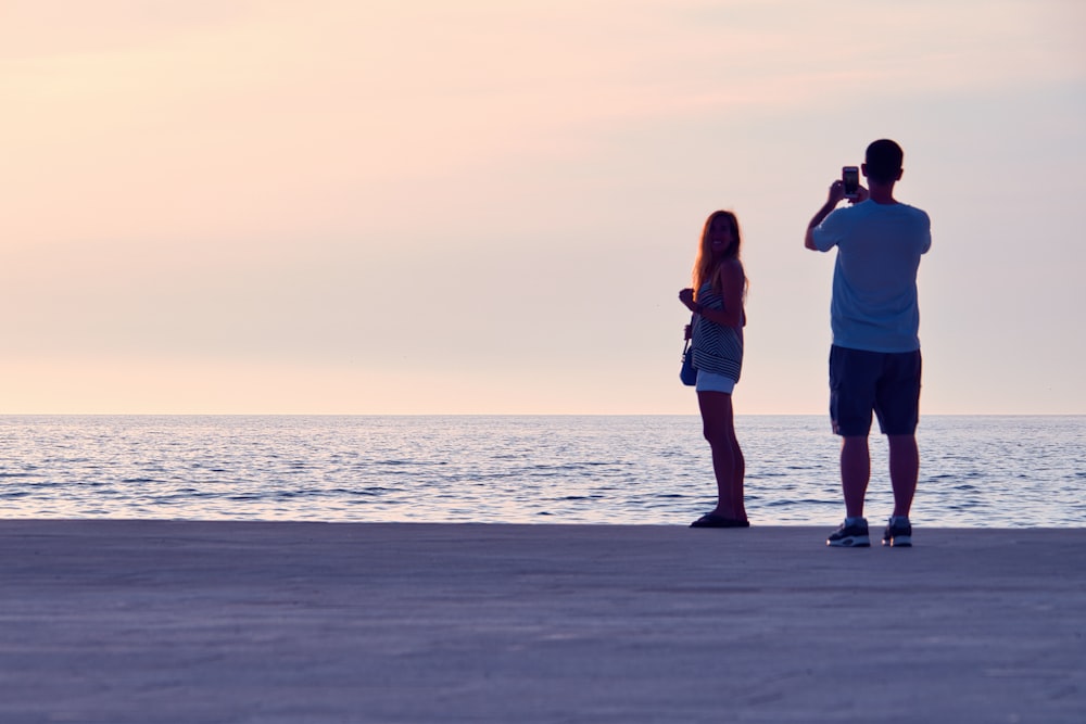 man and woman standing on beach during sunset