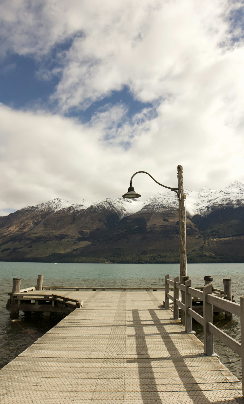 brown wooden dock near body of water and mountain under white clouds and blue sky during