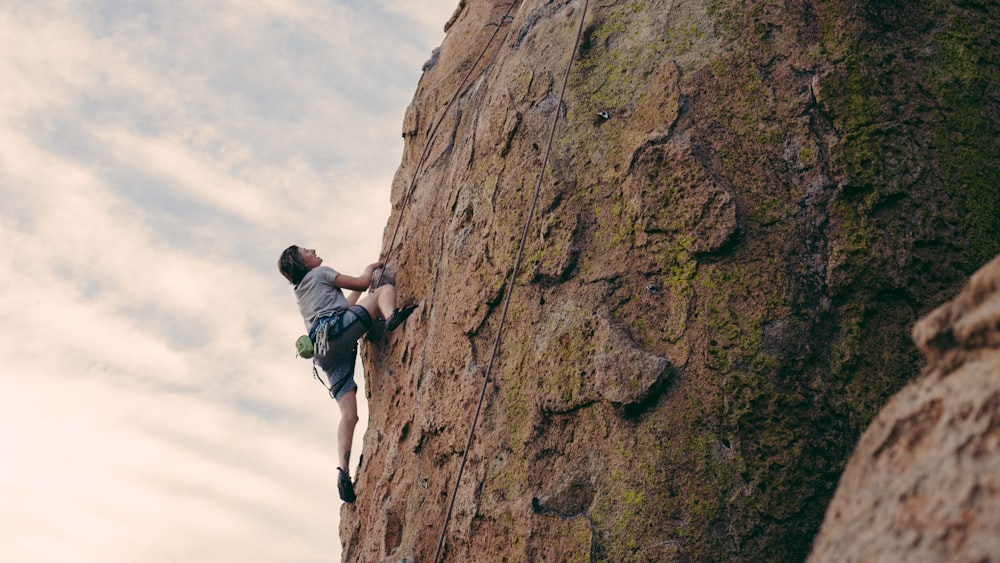 uomo in maglietta nera che si arrampica su roccia marrone durante il giorno