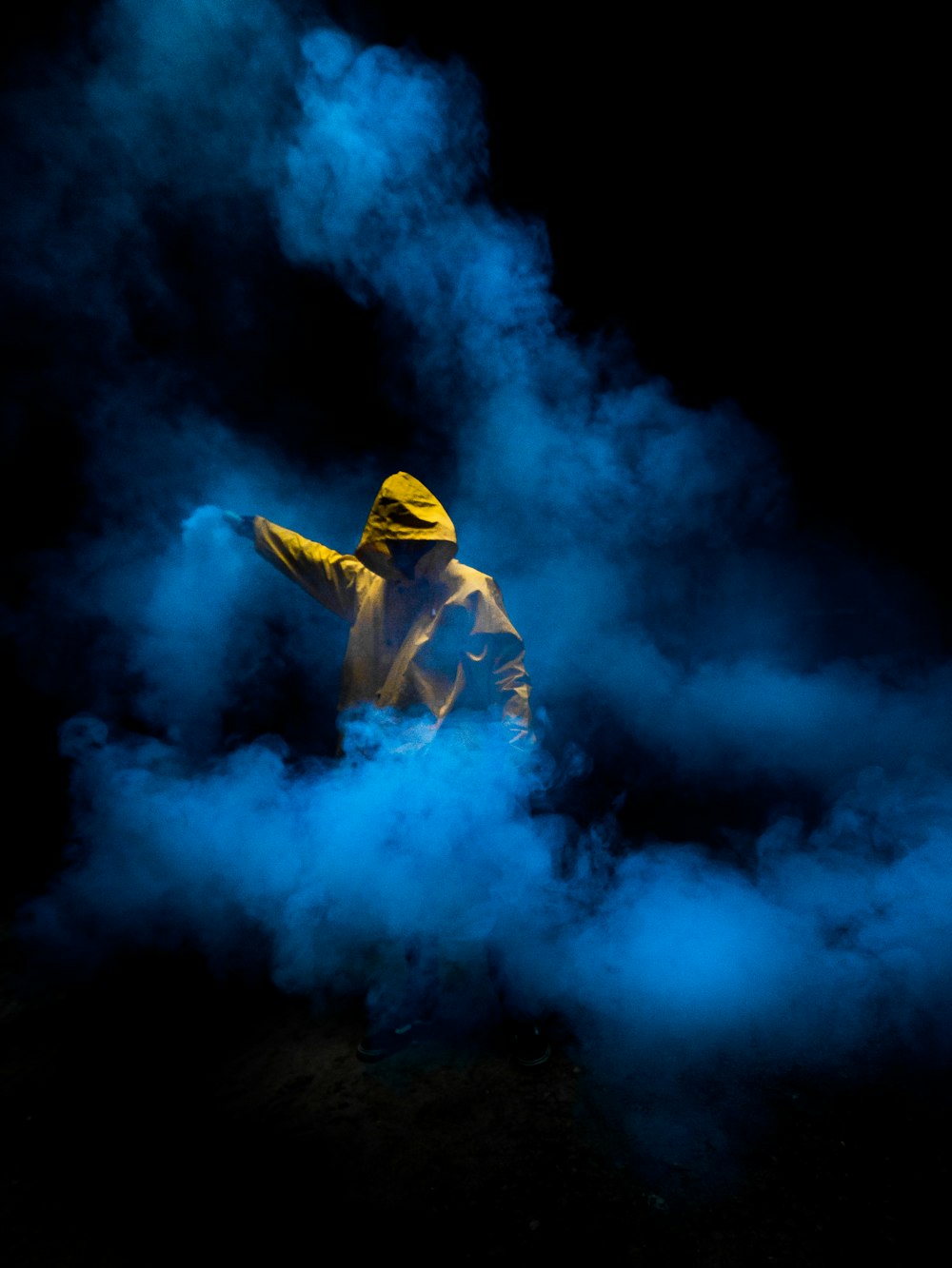 man in yellow hoodie and blue denim jeans standing on blue smoke