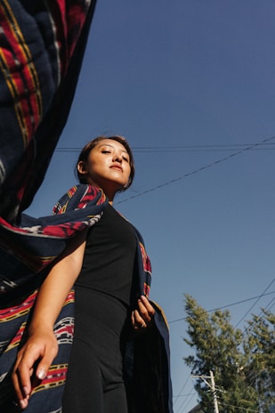A woman wrapped in a flowing midnight blue shawl, standing confidently with arms open under a starry sky.