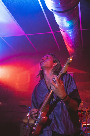 Pauric Mather playing guitar passionately on stage with warm lighting.
