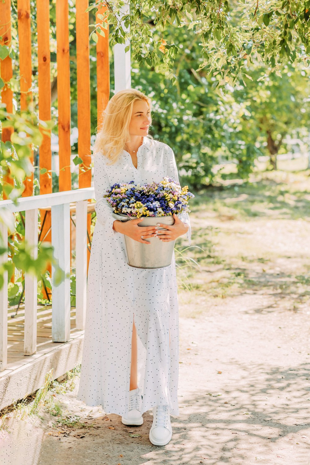 Mujer en vestido floral blanco y azul sosteniendo ramo de flores