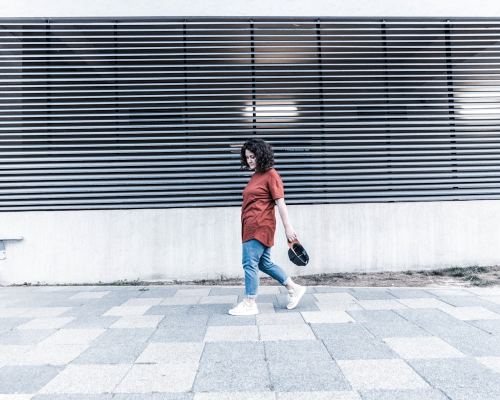 woman in orange t-shirt and blue denim jeans walking on sidewalk during daytime