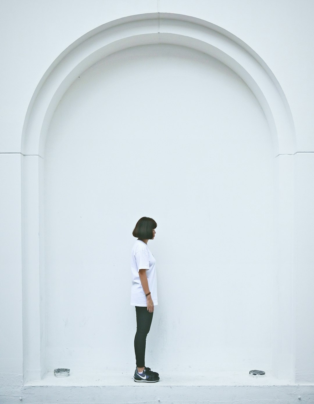 man in white t-shirt and black shorts standing in front of white wall