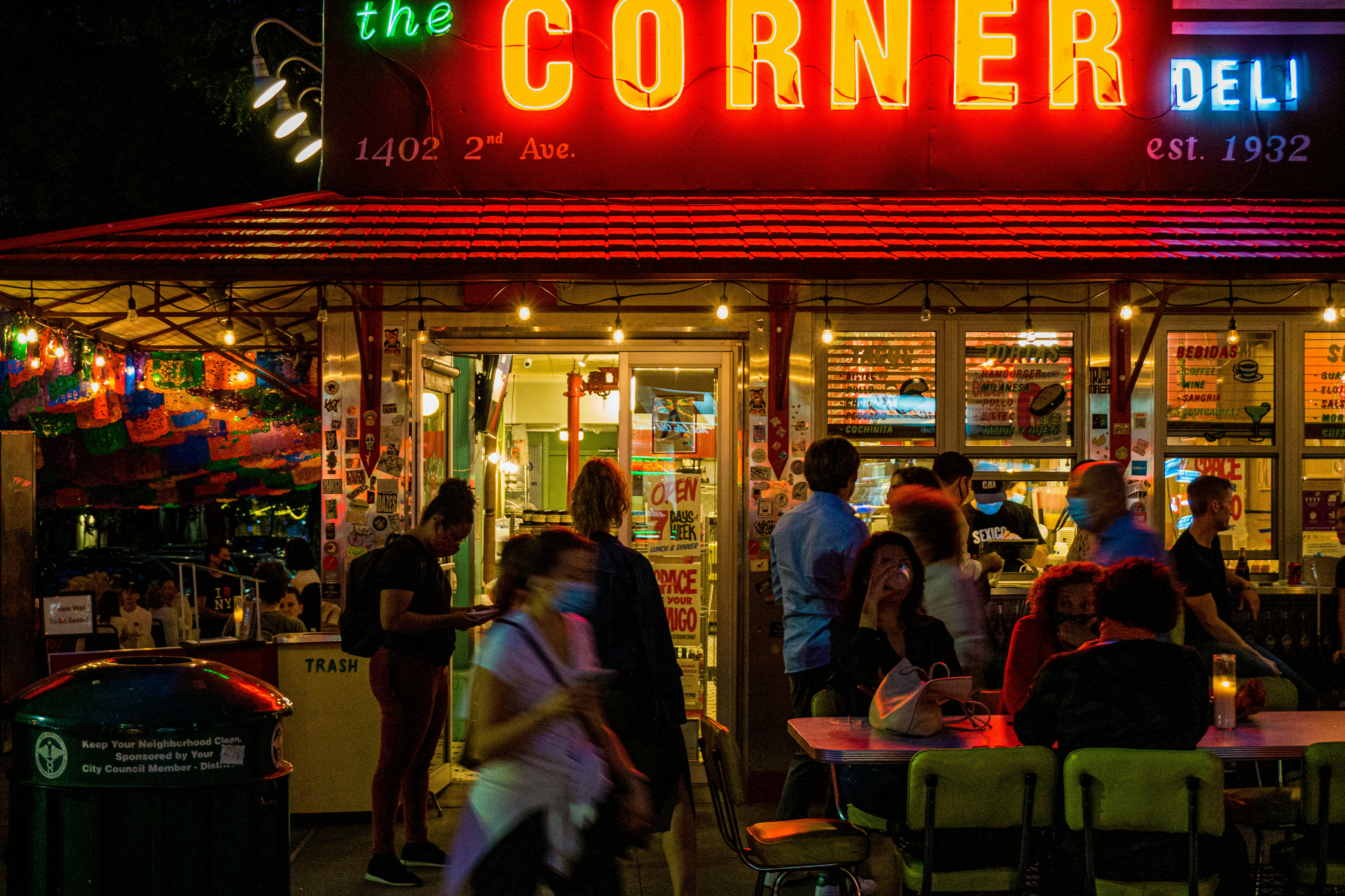 people sitting on chair in front of store during night time, Diners sitting at tables outside on the sidewalk due to COVID-19 banning indoor dining.