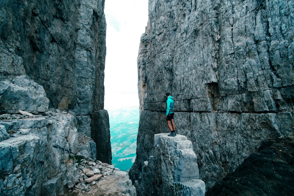 homme en chemise bleue et short bleu debout sur une formation rocheuse près d’un plan d’eau pendant