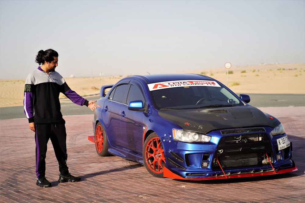 man in black jacket standing beside blue bmw m 3