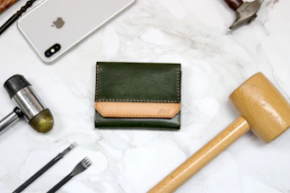 A warm wooden desk with leather crafting tools and a handmade leather wallet in progress.
