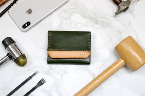 A warm wooden desk with leather crafting tools and a handmade leather wallet in progress.