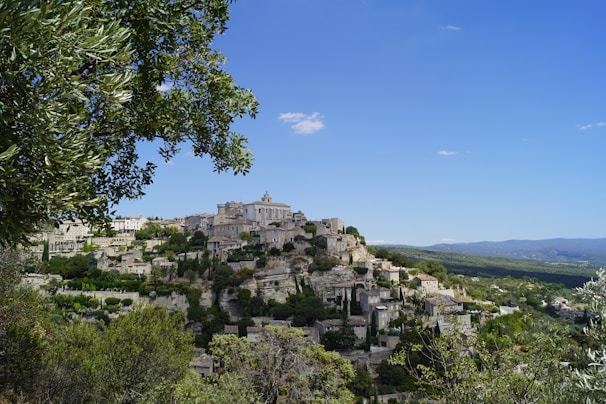 A peaceful village square with old stone buildings and locals sharing stories under olive trees.
