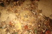 A richly detailed ceiling fresco filled with numerous angels and figures, depicted in dynamic poses and positioned around a central heavenly figure. The artwork features intricate patterns and a harmonious blend of colors, showcasing a sense of movement and divine presence.