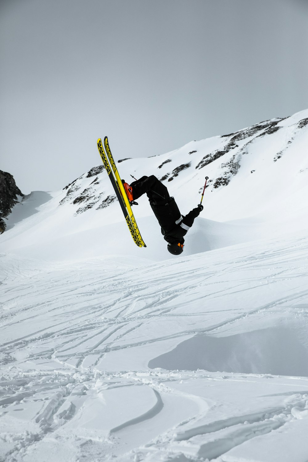 Hombre en chaqueta negra y pantalones negros montando una tabla de snowboard amarilla en la montaña cubierta de nieve durante el día