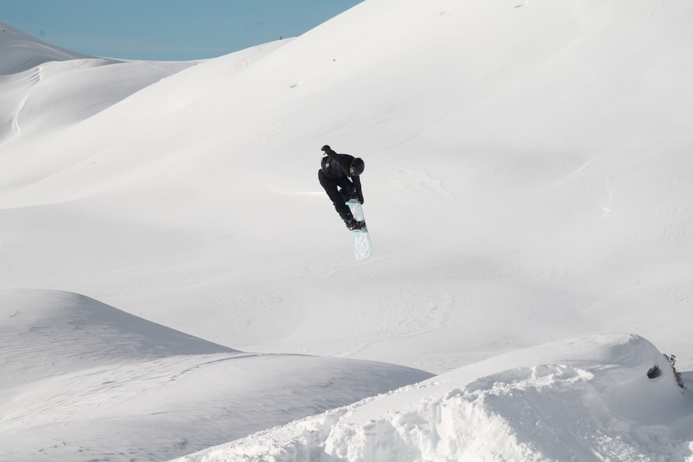 Mann in schwarzer Jacke und Hose geht tagsüber auf schneebedeckten Bergen