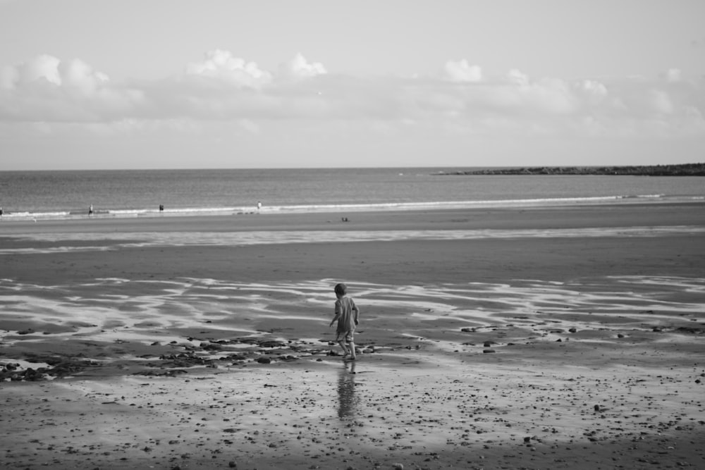 grayscale photo of person walking on beach