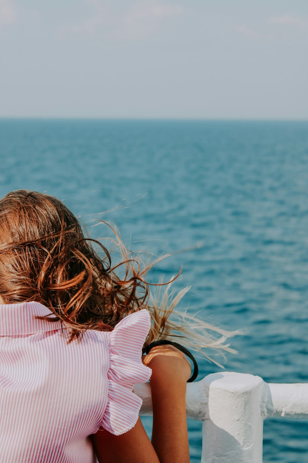 woman in pink shirt sitting on white chair near body of water during daytime