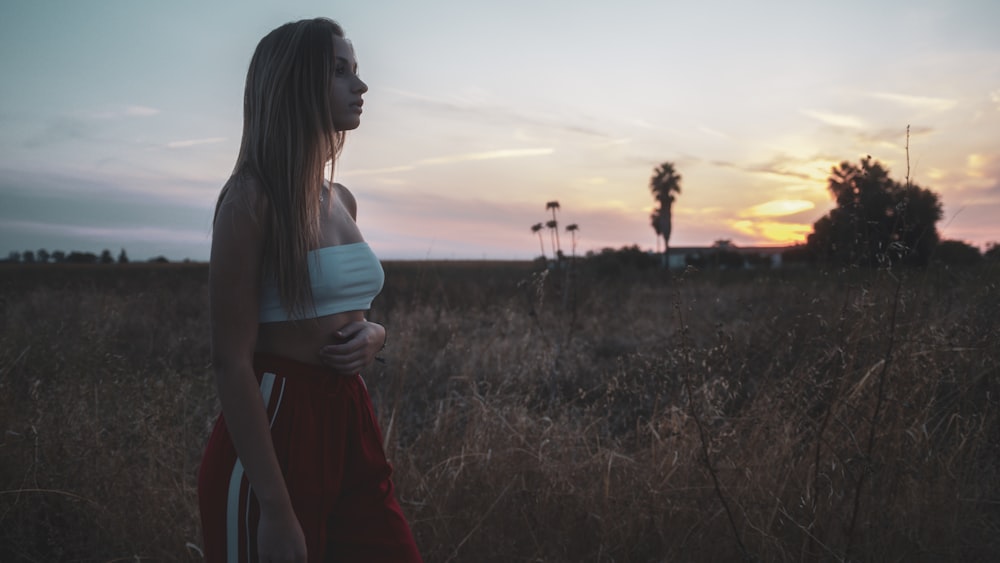 a woman standing in a field at sunset