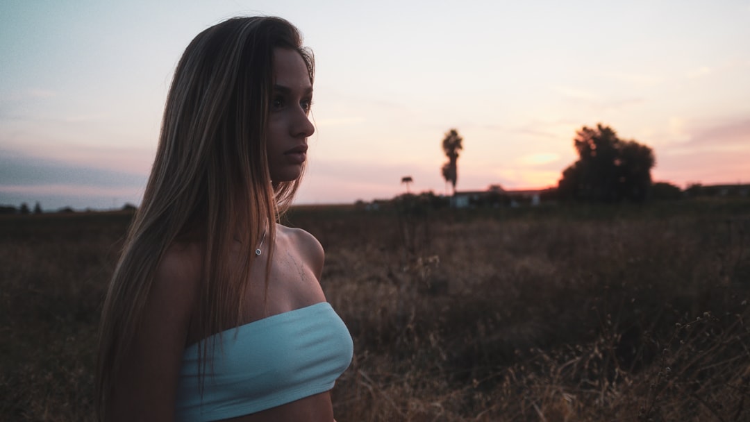 woman in white tank top and blue denim shorts standing on green grass field during sunset