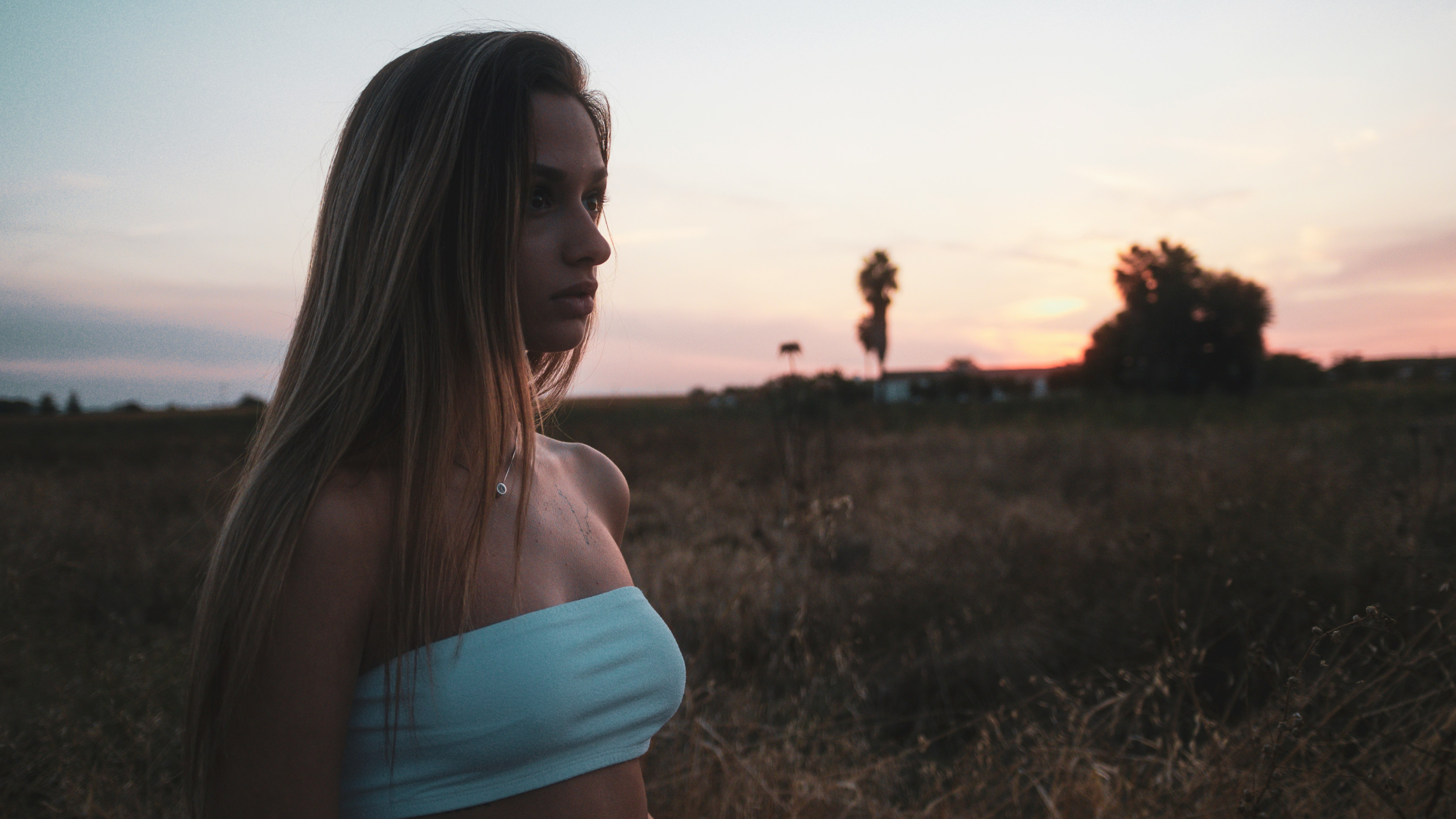 woman in white tank top and blue denim shorts standing on green grass field during sunset