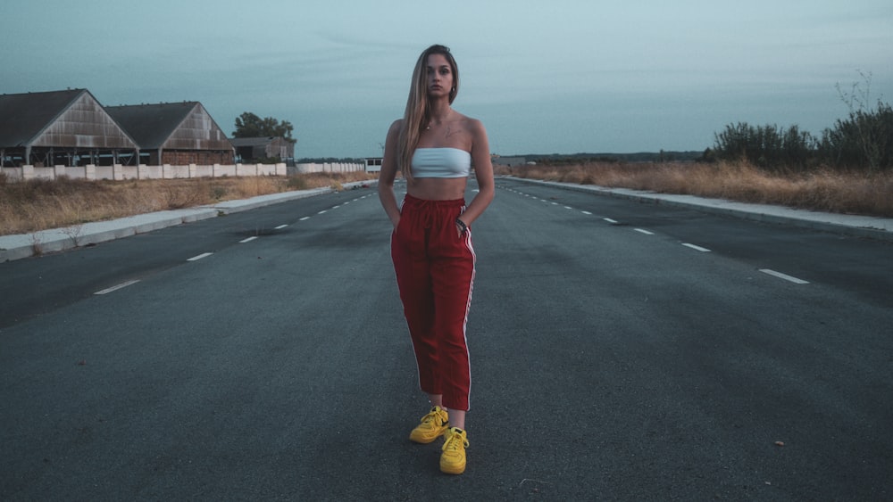 woman in white tank top and red pants standing on road during daytime