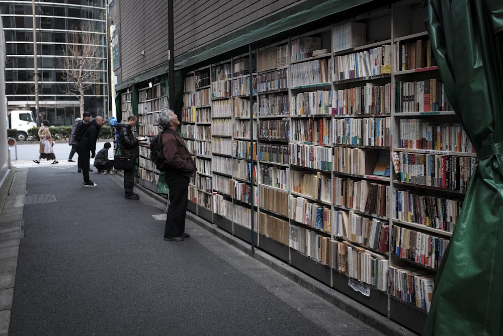 man in black jacket standing near books in book shelves