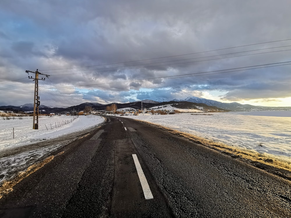 gray concrete road near body of water under white clouds and blue sky during daytime