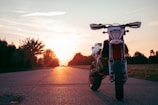 Side view of a rugged motorcycle parked on an open desert road at sunset.