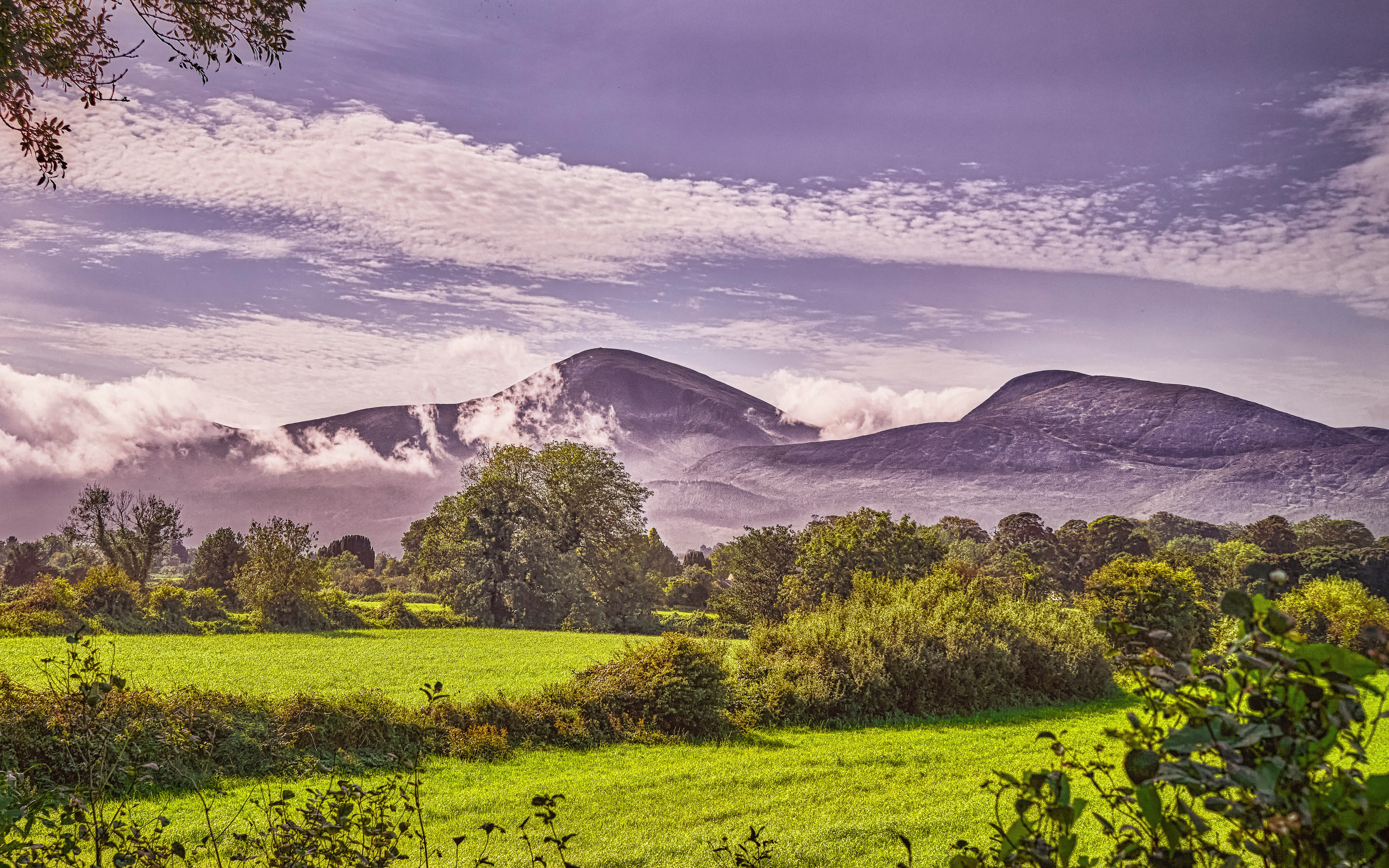 green grass field near mountain under white clouds during daytime