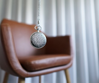 silver round pendant on brown wooden chair