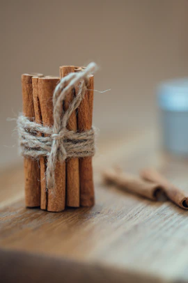 Close-up of cinnamon sticks bundled with rustic twine on a wooden surface.