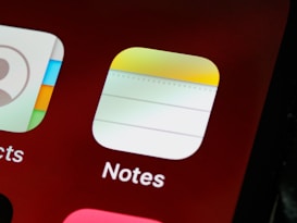 Close-up view of a smartphone screen displaying app icons, specifically the 'Notes' app with a notepad-like design and part of the 'Contacts' app icon visible.